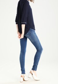 Blouse navy à manches trois-quarts avec bord blanc, associé à un jean skinny bleu et des talons ouverts blancs avec un talon carré.