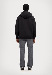 Felpa nera con cappuccio e vestibilità comoda, abbinata a jeans grigi. La felpa presenta polsini e orlo a costine, mentre i jeans hanno un taglio dritto.