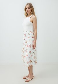 Weißes Spitzenkleid mit bunten Blumenmustern, A-Linien-Form, ärmelloses Design. Tragen mit beige gestreiften Sandalen. Solider Stoff-Oberteil.