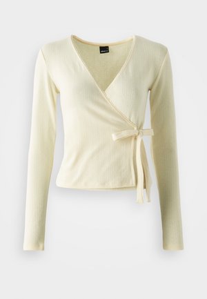 Krēmkrāsas garas piedurknes apvērts tops ar ribotu tekstūru un saitēm vidukļa daļā. V-veida dekoltē ar kontrastējošu apdari gar malām.