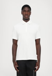Hvit polo skjorte med korte ermer, krage og treknapp-feste. Strukturert stoff, tettsittende design, kombinert med svarte bukser.