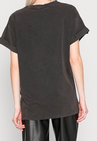 Camiseta de algodón negra oversized con mangas enrolladas, que muestra un ajuste relajado y una textura suave y mate. Diseño trasero simple, sin gráficos.