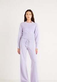 Σετ πλεκτής ρούχων για χαλάρωση σε λιλά χρώμα, που περιλαμβάνει ζακέτα με κουμπιά και παντελόνι με κορδόνι στη μέση. Μαλακή υφή και άνετη εφαρμογή με μακριά μανίκια και φαρδιά παντελόνια.