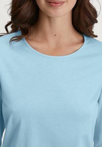 Lichtblauw langslieve shirt met een ronde hals. De stof lijkt zacht en glad, met een licht gestructureerd oppervlak.