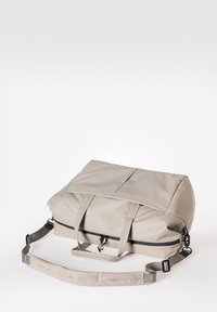 Beige Sporttasche aus robustem Stoff, ausgestattet mit zwei Griffen, einem verstellbaren Schultergurt und einem Reißverschluss mit einem schwarzen Akzent.