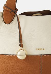 Sac à main en cuir beige et blanc avec une finition texturée, doté d'un charm rond en métal doré, d'accents cousus et du nom de marque embossé "Furla".