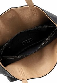 Sac fourre-tout en cuir noir avec un intérieur beige. Dispose d'une poche zippée et d'une couture détaillée. Design ouvert pour un accès facile au contenu.