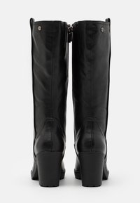 Bottes noires en cuir montantes avec un talon épais, présentant une texture lisse, des coutures verticales et une fermeture éclair à l'arrière.