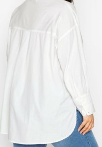 Vit långärmad skjorta med en något löst passform, som har en rundad nederkant, knappade manschetter och ett mjukt, texturerat tyg.