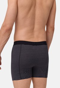 Boxer shorts rayés noir et gris avec une taille en noir comportant un texte en relief. Le tissu semble doux avec un ajustement snug.