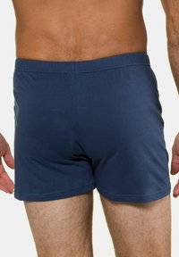 Donkerblauwe katoenen boxershorts met een elastische tailleband, voorzien van een gladde textuur en een minimalistisch ontwerp, gezien van achteren.
