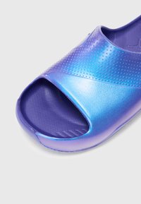 Lilla sklidesandal med en blank, teksturert finish. Åpen tå-design, med en glatt overdel med perforerte detaljer for pusteevne.