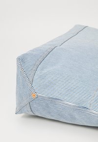 Striped cushion in blue and white, with visible stitching and a round orange button, features a soft textured fabric.