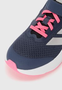 Chaussure de sport avec un dessus en maille marine, des lacets roses et une semelle blanche avec un accent rose. Surface texturée et coque renforcée à l'avant.