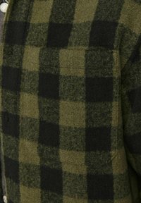 Roheline ja must ruuduline flanellide särk. Omab pehmet, tekstuurset kangast koos nööbiga ees ja rinnaeingiga taskuga. Nurgelised mustrid on silmapaistvad.