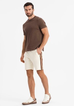 Brun bomuld T-shirt, creme shorts med brune sidelommer og brune og hvide sneakers. Casual pasform med minimalistisk design.