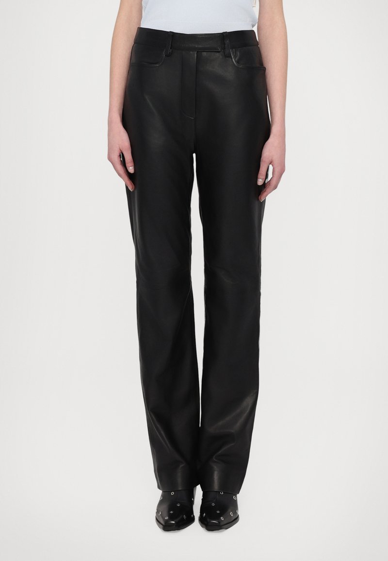 Pantalons en cuir noir avec une coupe droite, dotés de poches avant et arrière, et d'une texture lisse. Portés avec des chaussures noires ornées.
