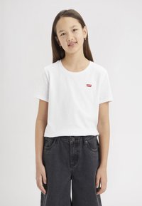 T-shirt bianco in cotone con scollatura rotonda e maniche corte, caratterizzato da un piccolo logo rosso di Levi's. Abbinato a jeans in denim grigio scuro.