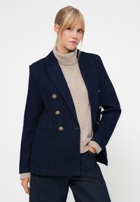 Marineblå dobbeltradet jakke med gullknapper, laget av strukturert stoff. Lange ermer, spisse slag og frontlommer.