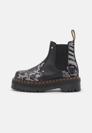 Botín Chelsea negro y gris con plataforma, suela gruesa, costuras amarillas, paneles laterales elásticos y detalles de estampado animal.