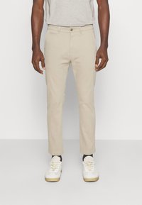 Beige chinos med raka ben, tillverkade av bomull, med framfickor och knäppning. Ihopkopplade med vita sneakers och svarta strumpor.