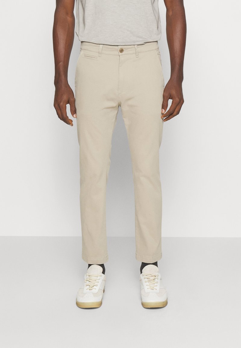 Beige chinos med raka ben, tillverkade av bomull, med framfickor och knäppning. Ihopkopplade med vita sneakers och svarta strumpor.