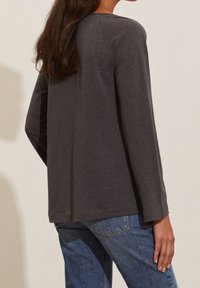 Grå långärmad skjorta i mjukt tyg, med rundad halsringning och något lös passform, tillsammans med denimjeans.