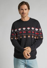 Granatowy sweter dziany z świątecznym wzorem przedstawiającym Świętego Mikołaja, renifery i ciężarówki w czerwieni i bieli na wysokości klatki piersiowej, z fakturą warkocza.