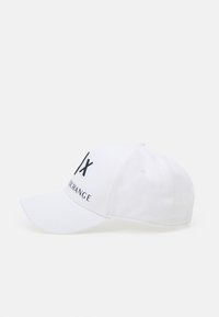 Hvit baseballcap med buet brem, med svart trykt tekst "IX" og "EXCHANGE" på frontpanelet. Laget av bomullsstoff.