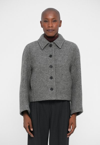 Gray wool jacket with a collared neckline, featuring six black buttons, cropped design, and long sleeves. Worn with pinstriped trousers.