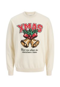 Crème trui met een gebreid ontwerp met "XMAS" in het rood, hulst en bellen. Onder de tekst staat: "Stuur me een bericht wanneer het kersttijd is."