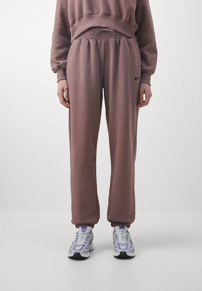 Pantalones deportivos rosas con cintura elástica, bolsillos laterales y puños acanalados, combinados con zapatillas blancas y moradas.