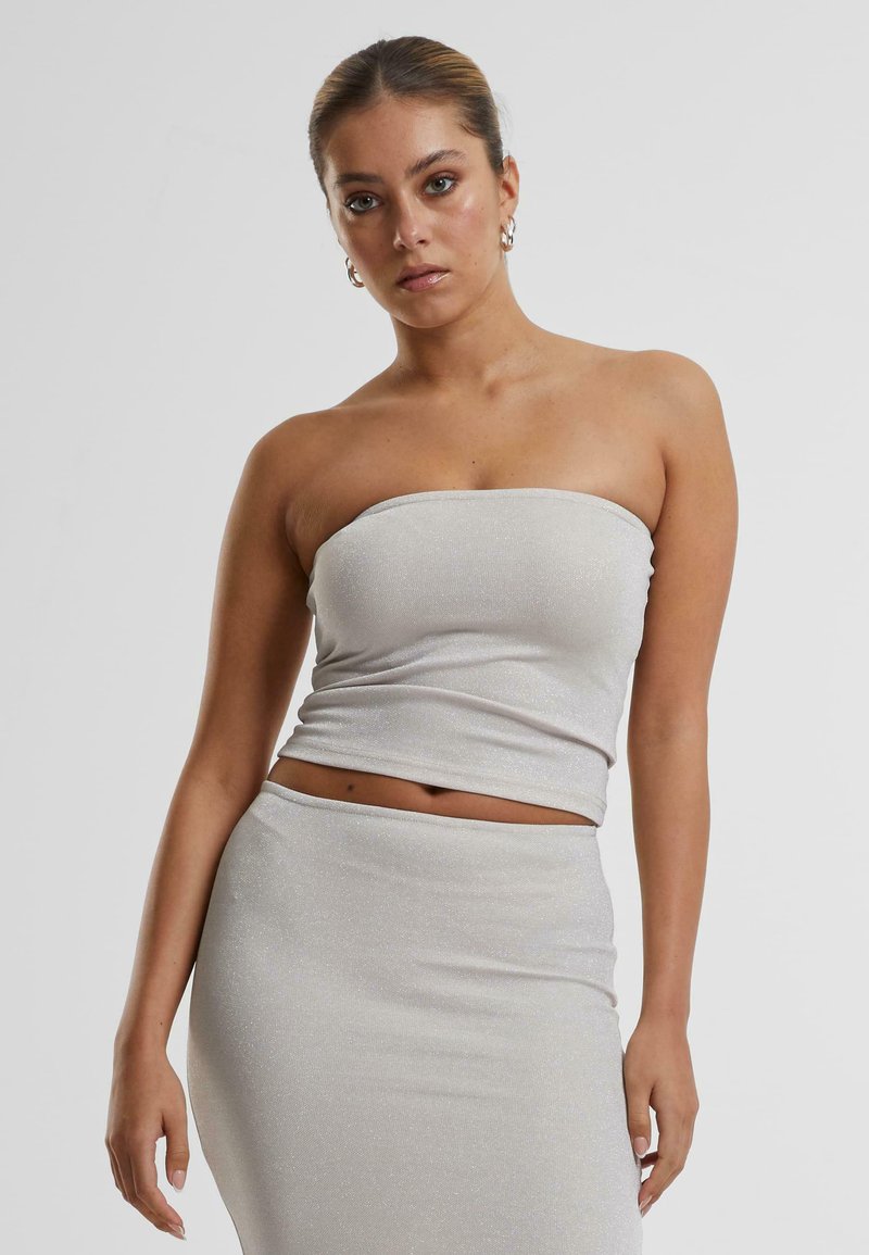 Haut argenté à côtes, sans bretelles, avec une texture lisse, conçu pour épouser les formes. Associé à une jupe crayon ajustée et assortie.