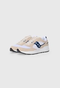 Beige athletic sneakers with mesh, suede, and rubber materials. Features navy accents, white branding, and a textured sole.