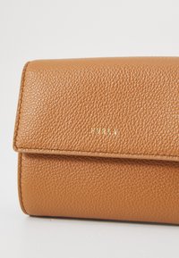 Portefeuille en cuir brun à texture granuleuse, avec un logo doré en relief. Design de forme plate et rectangulaire avec une fermeture à rabat.