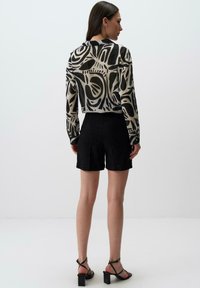 Blusa trasparente e tagliata con un motivo astratto in bianco e nero, abbinata a shorts neri a vita alta. Modella con sandali neri con cinturini.