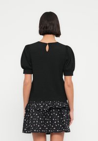 Μαύρο, υφασμάτινο τοπ με κοντά μανίκια και φουσκωτά μανίκια, με λεπτομέρεια πίσω με άνοιγμα σε σχήμα κλειδιού, συνδυασμένο με ρουμπάτο φόρεμα με floral σχέδιο.