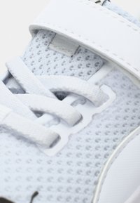 Helle graue Sneaker mit einem atmungsaktiven Mesh-Obermaterial, flachen weißen Schnürsenkeln und einem Klettverschluss. Strukturiert Oberfläche mit dezenten Nähdetails.