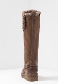 Wysoki, brązowy zamszowy botek zimowy z futrzanym wykończeniem, bocznym zamkiem, dekoracyjnym paskiem z klamrą i teksturowaną, stalową podeszwą z wytłoczonymi ćwiekami.