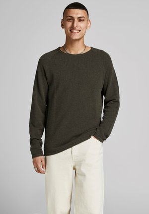 Camisa de punto de manga larga verde oscuro con cuello redondo y puños de canalé, combinada con pantalones beige claros. Diseño simple y texturizado.