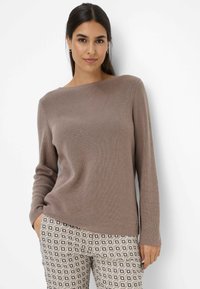 Pull marron à côtes avec un large col et des manches longues, associé à un pantalon à motifs présentant des designs géométriques dans des tons beiges et marron.
