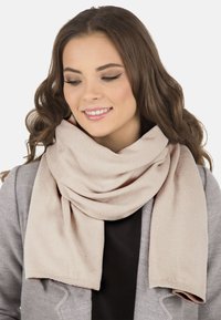 Eșarfă tricotată bej, așezată delicat în jurul gâtului, cu o textură netedă și un design relaxat, supradimensionat.