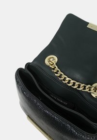 Borsa nera in pelle con un finish texture, dettagli in catena dorata e una chiusura metallica. Sono visibili i compartimenti interni.