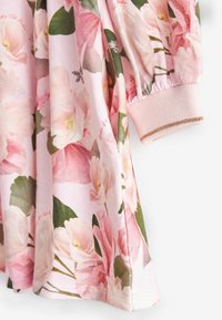 Tissu fleuri rose avec des feuilles vertes, doté d'un poignet froncé avec un détail de bande dorée sur la manche longue.
