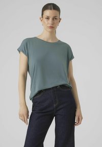 Korte mouwen teal t-shirt van zacht materiaal, met een ronde halslijn en een ontspannen pasvorm, gecombineerd met donkerblauwe high-waisted jeans.