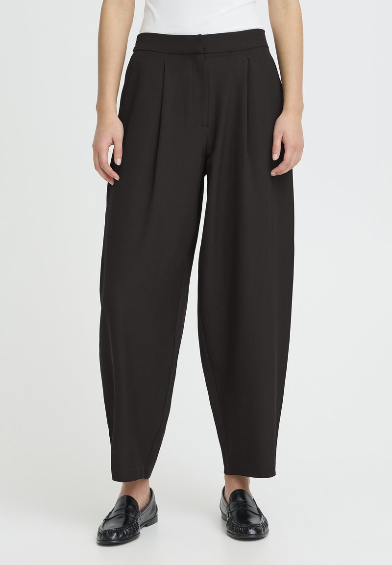 Pantalones negros plisados hechos de tela suave, con una cintura alta y piernas anchas. Combinados con mocasines negros.