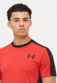 Rød atletisk skjorte med svarte detaljer, fukttransporterende stoff, korte ermer og rund halsutskjæring. Har en logo på brystet.