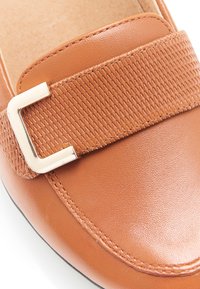 Mocassino in pelle marrone con una fascia testurizzata e una fibbia rettangolare in argento. Superficie liscia con dettagli di cuciture.