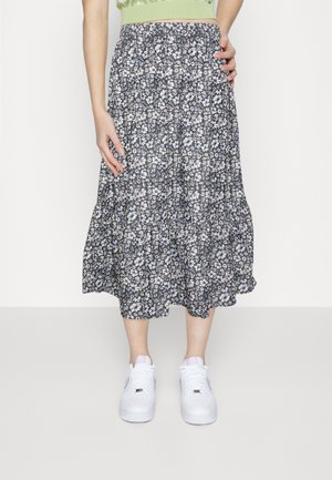 Falda midi floral en azul marino con flores blancas y celestes. Tejido ligero, diseño en capas, cintura elástica, combinada con zapatillas blancas.