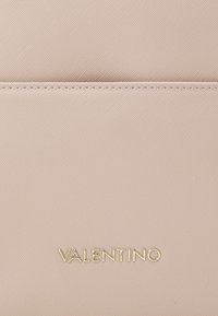 Ljusrosa läderväska med texturerad yta. Guld "VALENTINO"-logotyp längst ner. Minimalistisk design med en jämn yta utan extra dekorationer.